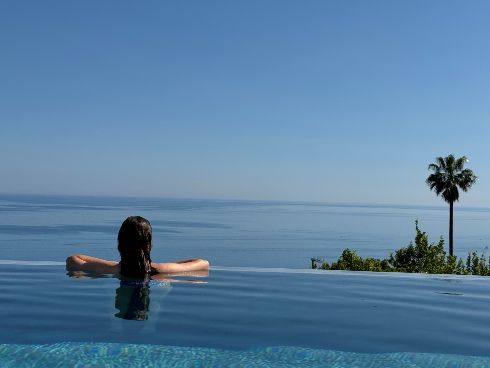 Woman relaxing in infinity pool with sea view